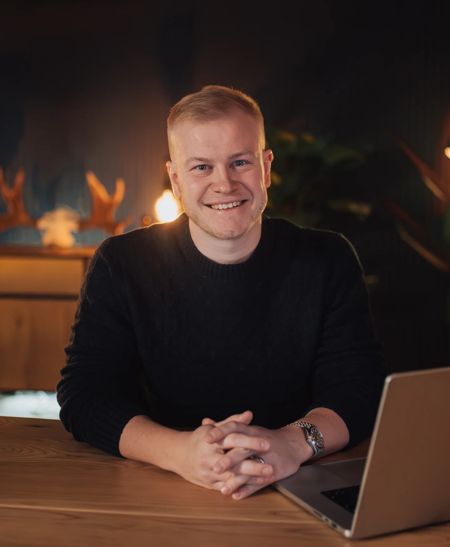Gusten Sun smiling at his studio desk, wearing a dark sweater